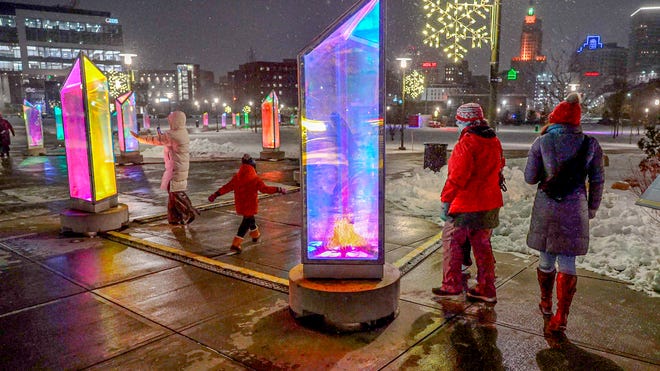 Families enjoying the Prismatica art installation at the LUMINA Light Festival, featuring colorful illuminated prisms on a snowy winter evening in a city plaza.