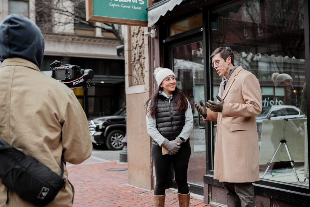 Providence Mayor Brett Smiley talks with DPPN Executive Director Nora Barré outside a storefront, while being filmed.