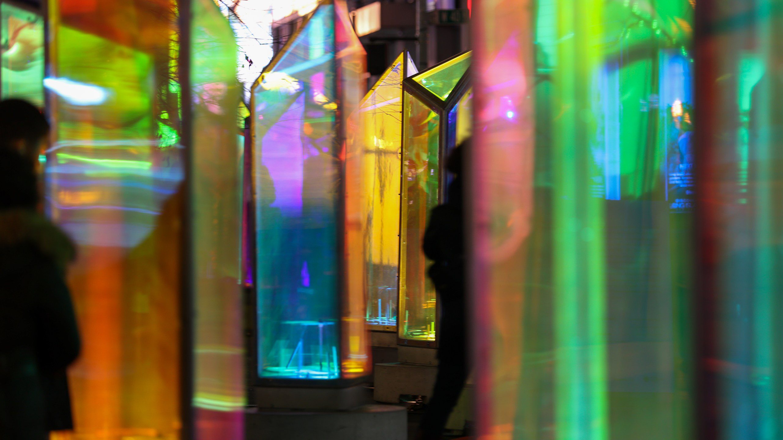 Colorful illuminated art installation with vibrant glass-like panels reflecting rainbow hues, captured at the LUMINA Light Festival.