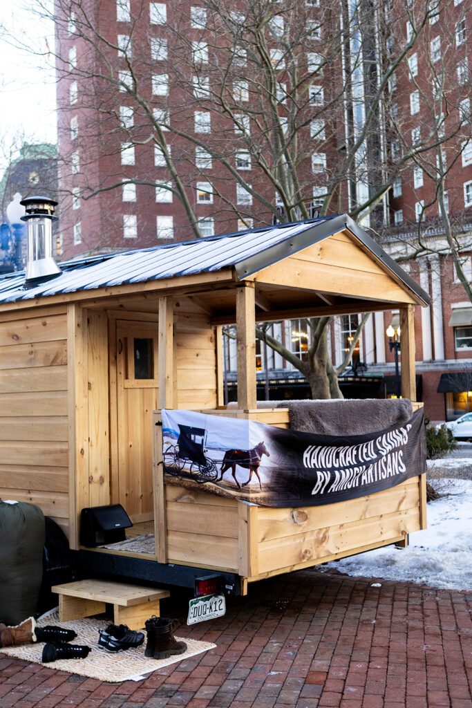 The LUMINA Mobile Sauna is parked on brick pavement with a backdrop of a tall building.