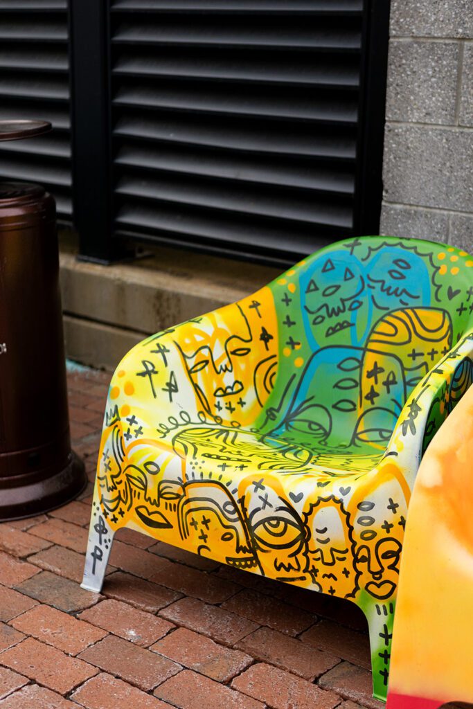 Colorful chair with abstract face designs on a brick patio.