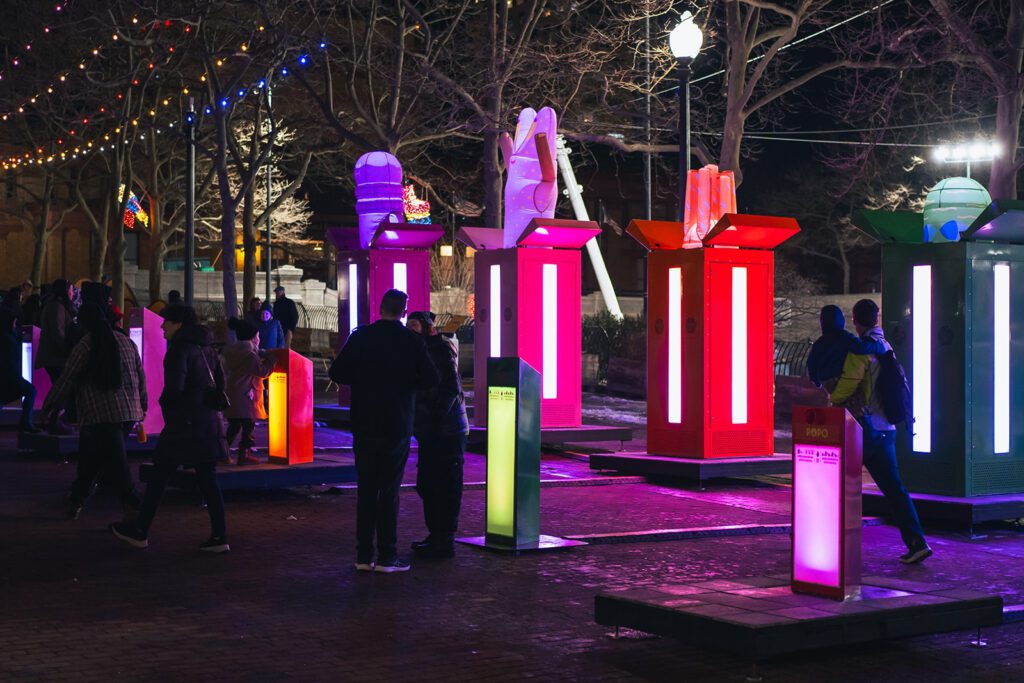 People enjoying the colorful light installations of POP! by Gentilhomme at LUMINA, set against a backdrop of illuminated trees.