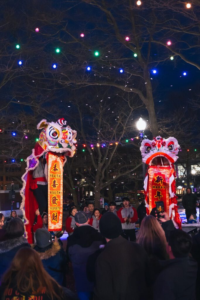 Lion dance performance with colorful lights and crowd during a festive night celebration.