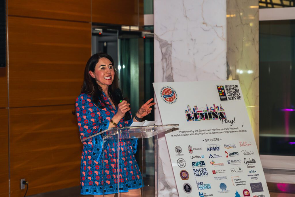 Downtown Providence Parks Network Executive Director Nora Barré speaks at a podium beside a LUMINA event sign.