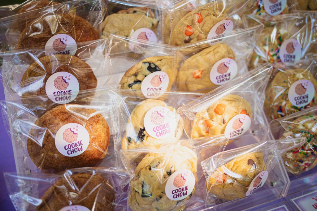 Assorted cookies from Cookie Chow, individually packaged in clear wrapping with branded stickers, featuring a variety of flavors such as snickerdoodle, sprinkle, and chocolate chip.