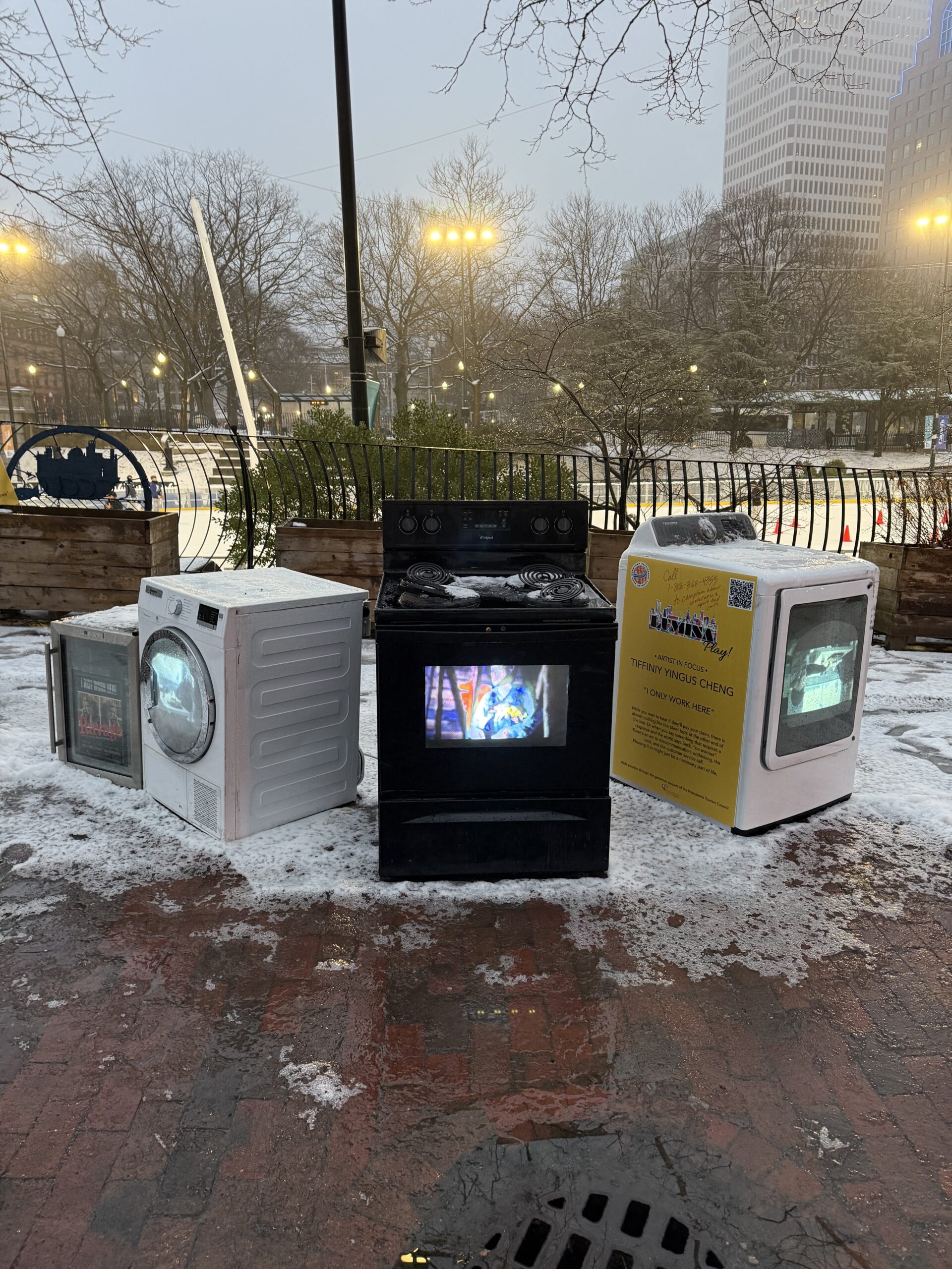 “I Only Work Here” by Tiffiniy Yingus Cheng, a public art installation featuring repurposed appliances with video screens in a snowy city park.